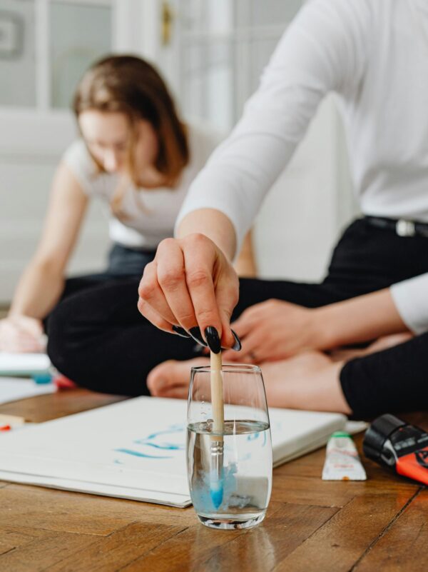 Woman dips paintbrush in water while engaging in artistic creativity at home.